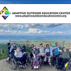 A group of people using wheelchairs with their arms raised in front of a view of mountains and lakes behind them; text: Adaptive Outdoor Education Center, www.adaptiveoutdooreducationcenter.org