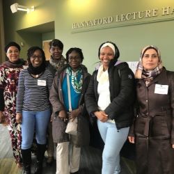 Six people smiling in front of the Hannaford Lecture Hall sign