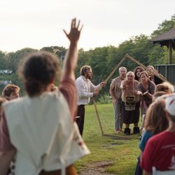 A group of people reach through a wooden pentagon to a person raising their hand