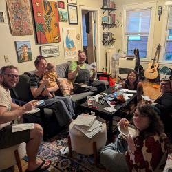 A group of people gathered around a table, enjoying a meal together and writing postcards.