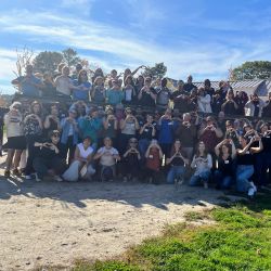 A large group of people make hearts with their hands while gathering outside.