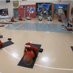 Several people stretch on yoga mats in a gymnasium with their faces blurred