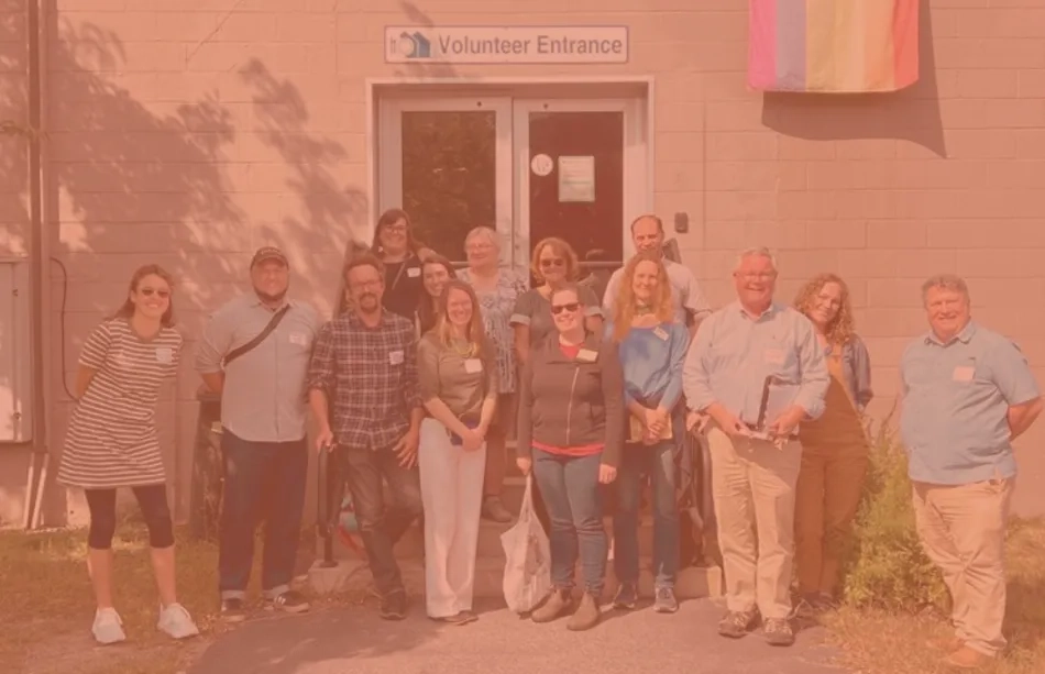 Group of people smiling at the camera outside a building with a sign for the Volunteer Entrance