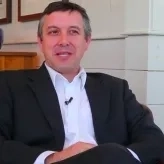 Photo of Colin Woodard sitting, white man with short brown hair wearing a white collared shirt and dark gray blazer in front of a white wall