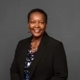 Idella smiling with a black blazer and long necklace