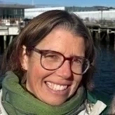 photo of a woman smiling. she is wearing glasses and a green scarf.