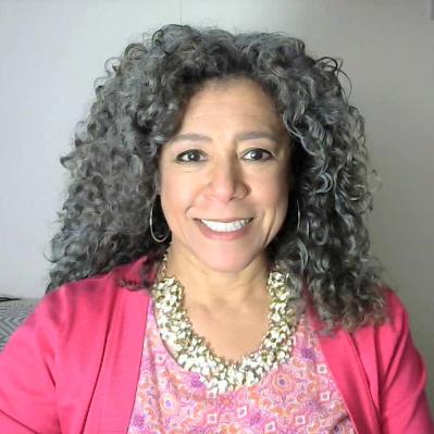 Lelia with a big smile wearing a pink cardigan and intricate necklace