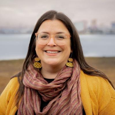 White woman with dark brown hair and glasses in a yellow sweater.